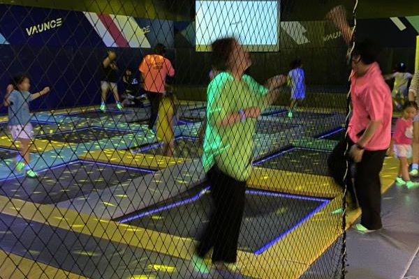 Grown-ups and children bounce on trampolines under neon laser lights. (Hwang Joo-young/The Korea Herald)