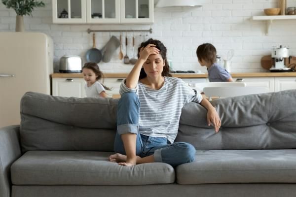 一位疲惫的女人坐在沙发上，孩子们在她身后奔跑